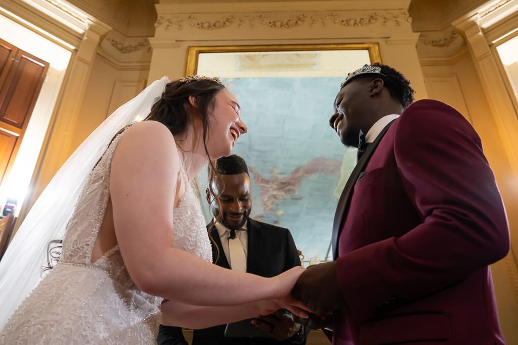 Couple smile during ceremony with ceiling view of the old Wyethtootle Mansion in Saint Joseph near Kansas City