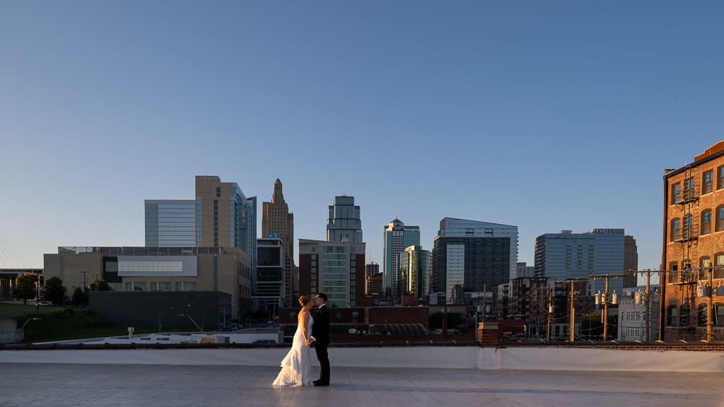 Couple kissing in front of the majestic Kansas City skyline at golden hour on the rooftop of Union Kansas City