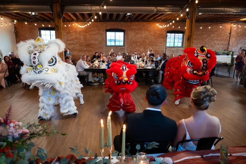 Three lion dancers looking at the couple during a Vietnamese multicultural wedding at Union Kansas City, with guests in the background