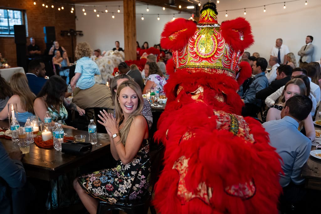 Lion dancer moving between guest tables during a Vietnamese multicultural wedding at Union Kansas City, with a woman with a big smile