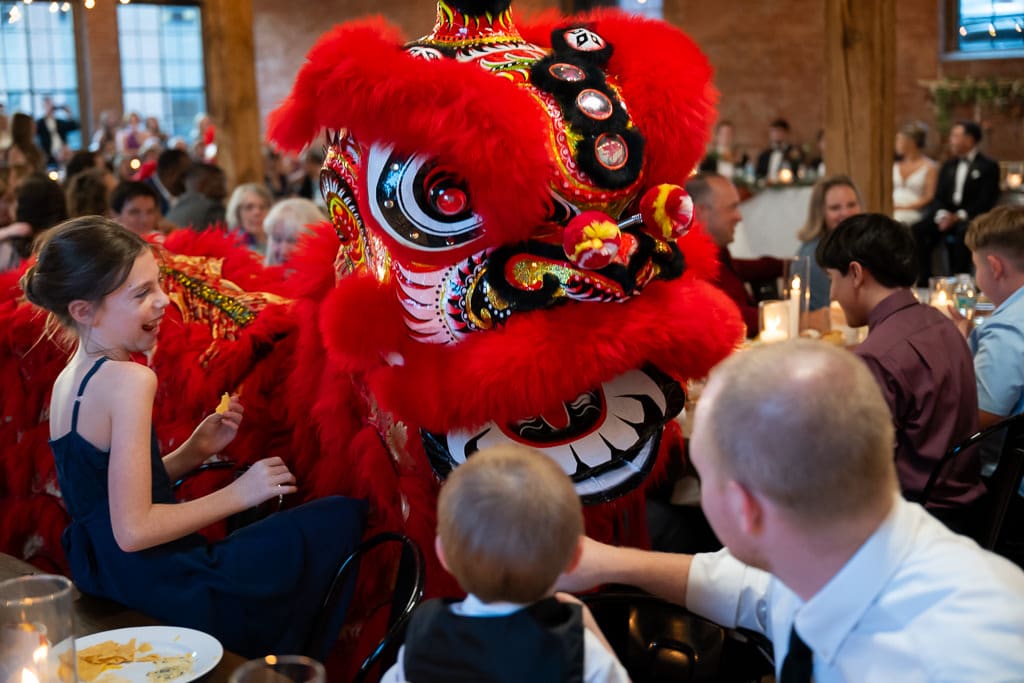 Lion dancer moving between guest tables during a Vietnamese multicultural wedding at Union Kansas City, with a child laughing