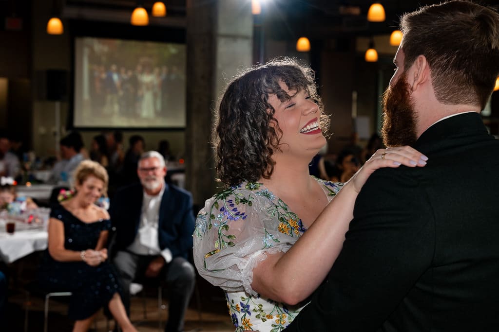 Bride laughing during her first dance with the groom as guests watch at Boulevard Brewing Company