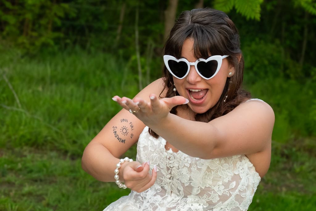 Bride in heart sunglasses reaching toward the camera at her Briar Creek Farms wedding