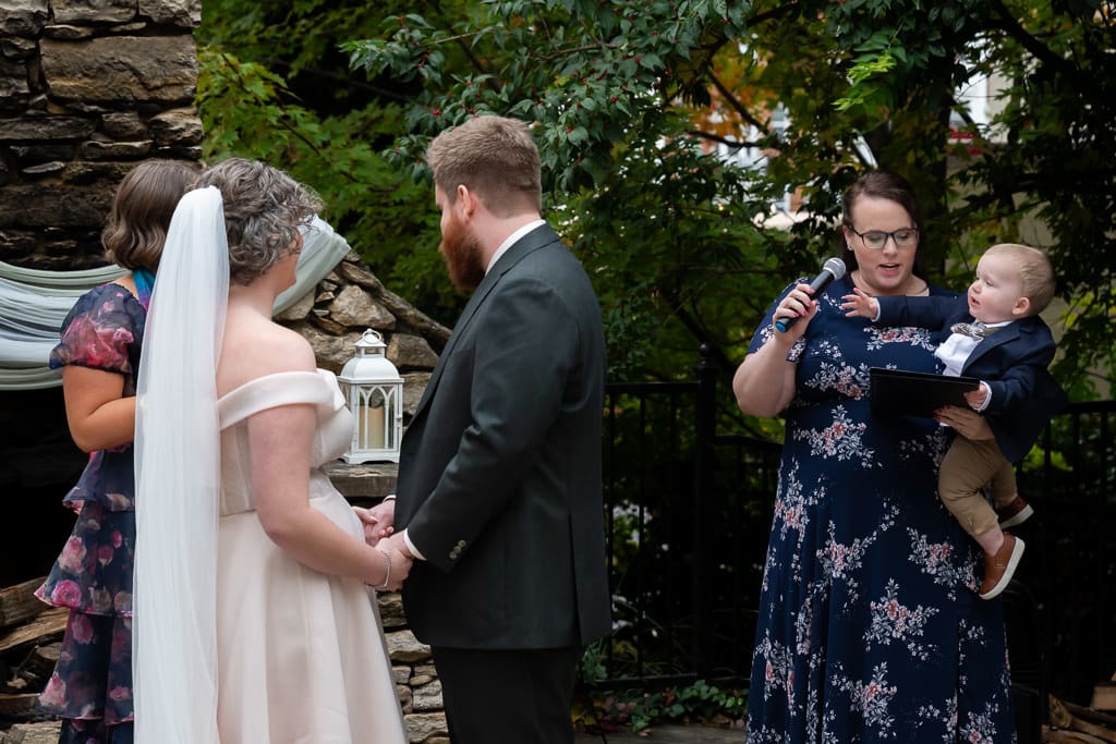 Child trying to hold the microphone of the speaker as the bride and groom hold hands during the ceremony
