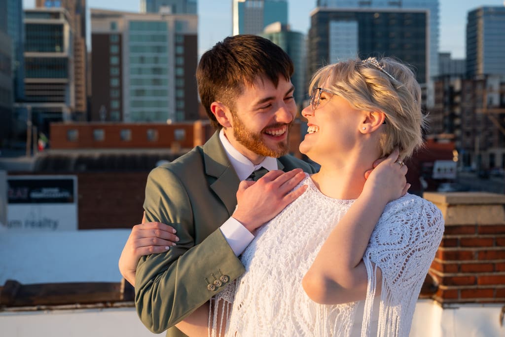 Bride and groom laughing together on a rooftop with the downtown Kansas City skyline behind them