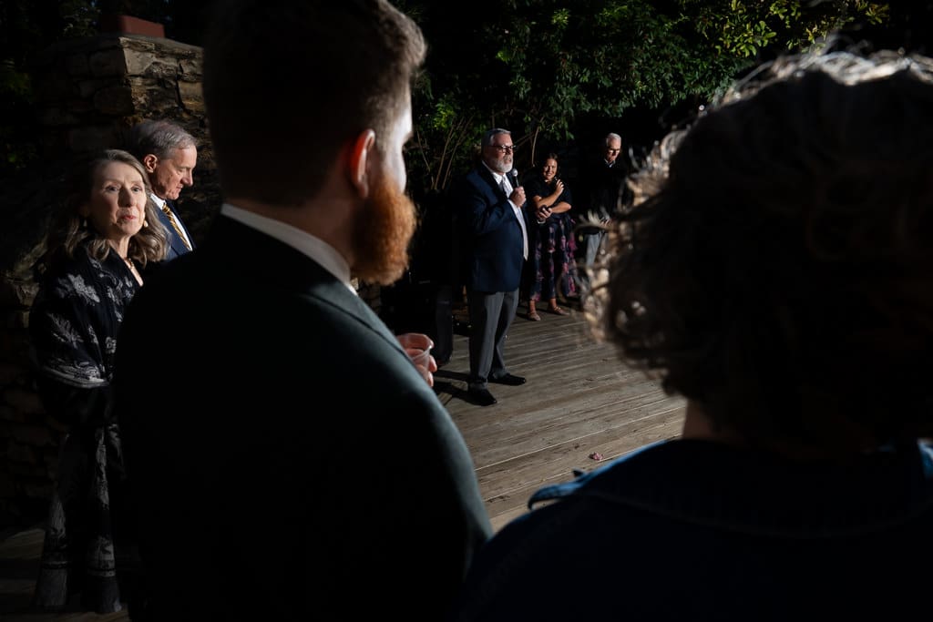 Groom watching the father of the bride's speech from the shadows of the garden