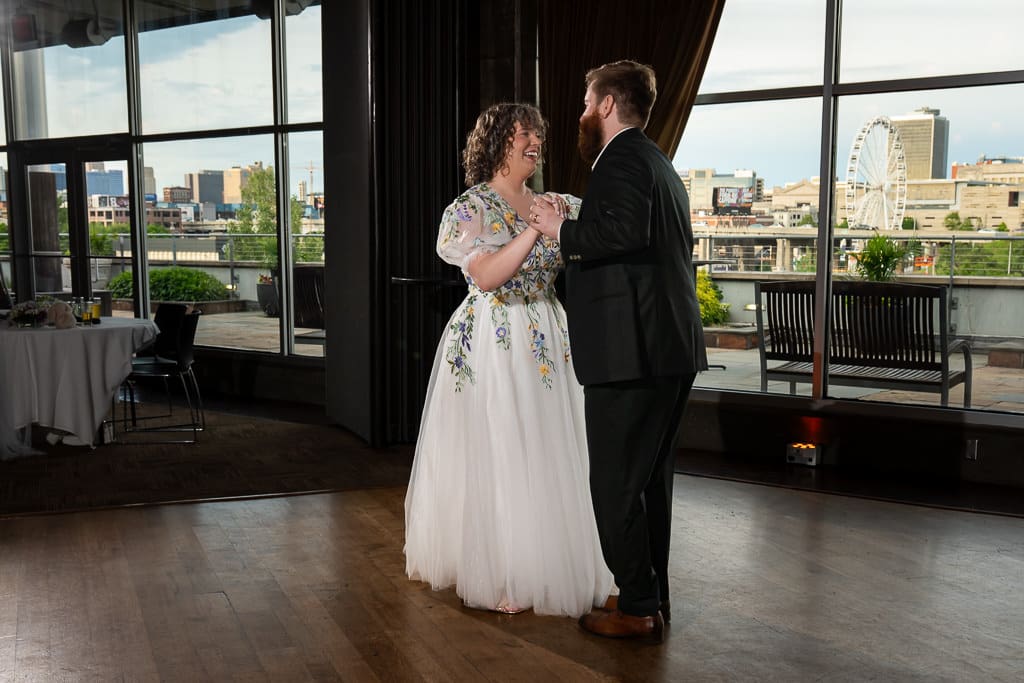 Bride and groom sharing their first dance by the windows with a Kansas City skyline view at Boulevard Brewing Company