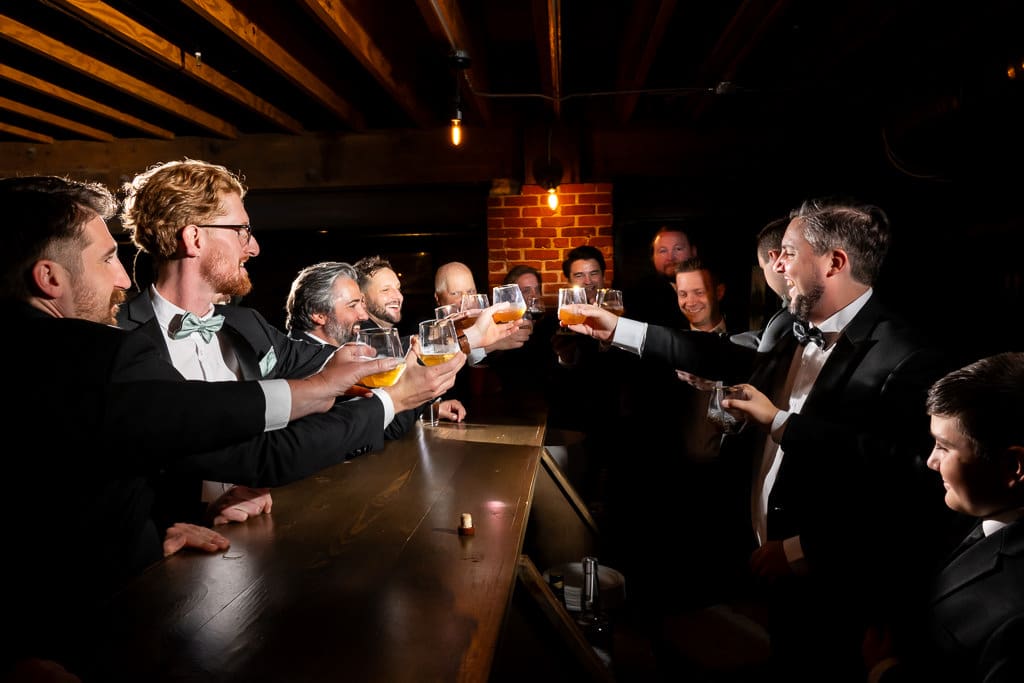 Groomsmen raising their whiskey glasses in a toast at the bar of the Union speakeasy room