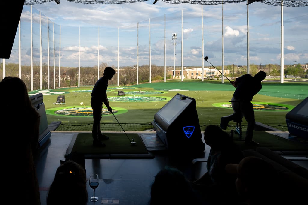 Wedding guests hitting golf balls over the driving range at a Topgolf wedding in Overland Park