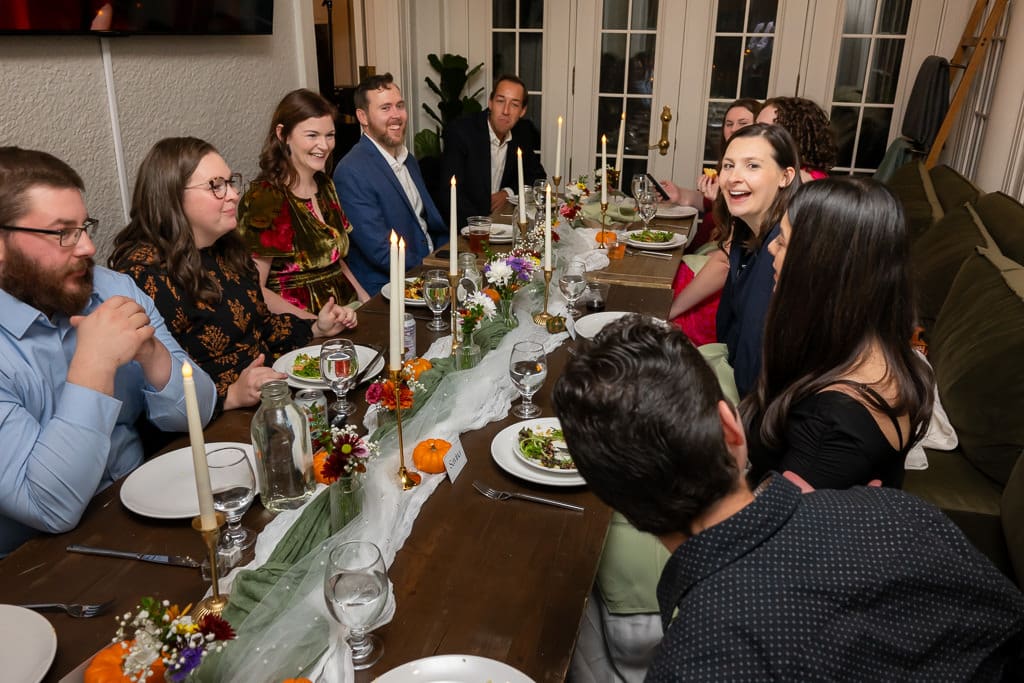 Wedding guests talking and laughing around a long candlelit dinner table at an intimate wedding at Southmoreland on the Plaza
