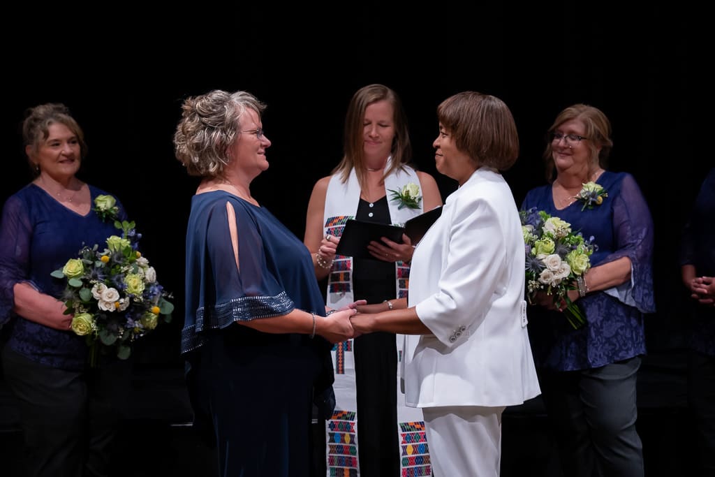 Two brides holding hands in front of their officiant and bridesmaids at their LGBTQ wedding in Kansas City