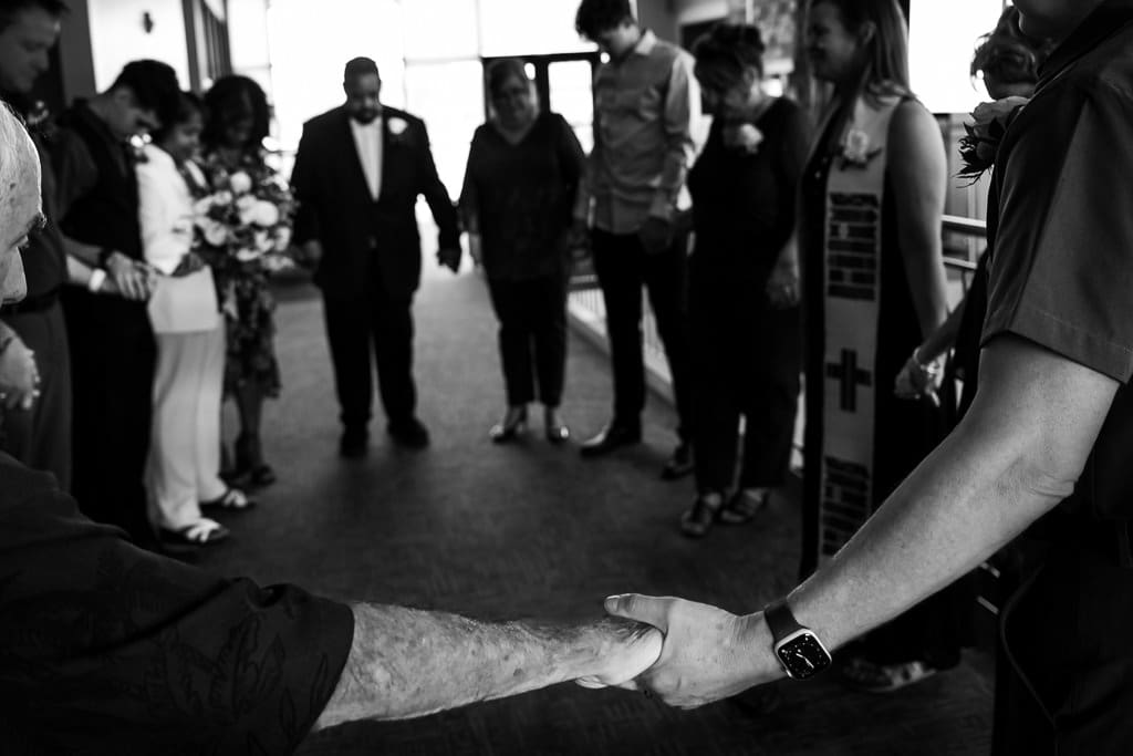 Black and white image of guests joining hands in a circle during a lesbian wedding ceremony in Kansas