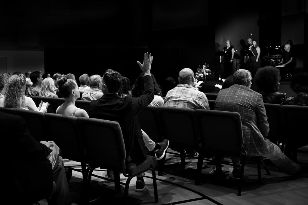 Black and white image of a guest waving hello to a friend across the room before an LGBTQ wedding ceremony in Kansas City