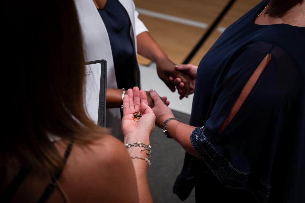 Wedding rings resting in the officiant's hand as the two brides hold hands behind during their lesbian wedding in Kansas