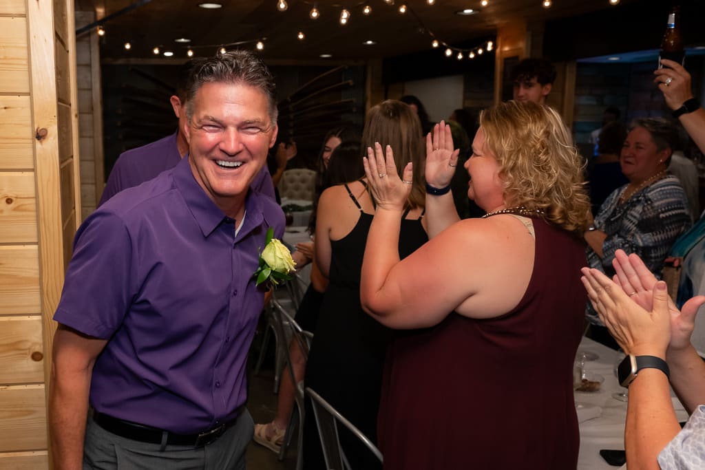 Guest smiling as friends cheer and clap at the wedding reception for Jacqueline and Shonda