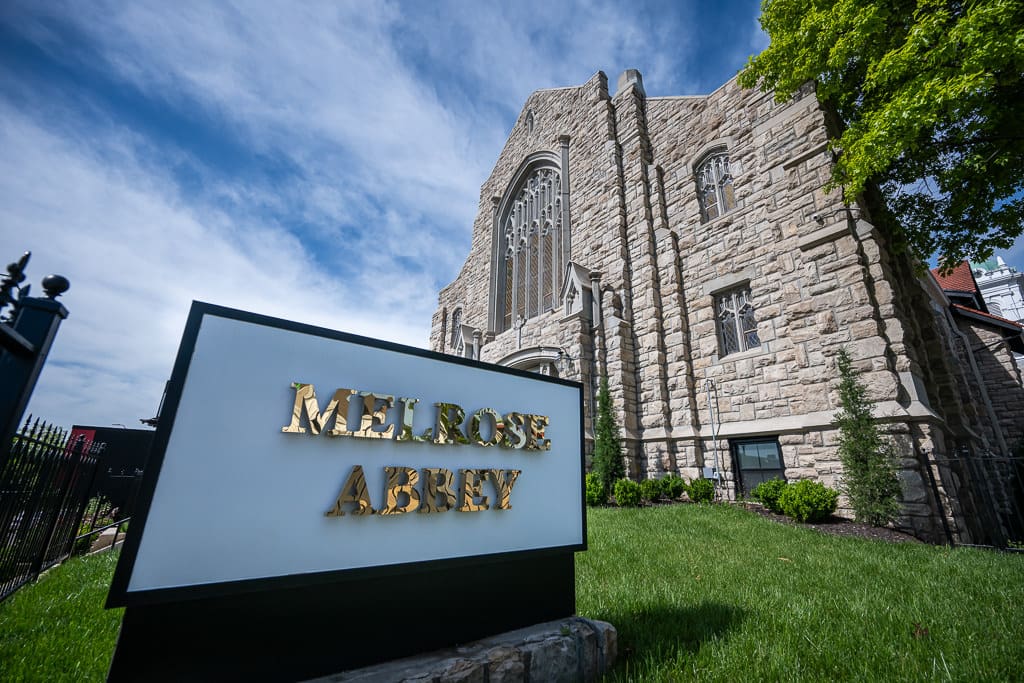 Melrose Abbey sign in front of the venue's stone Gothic church building under a blue sky