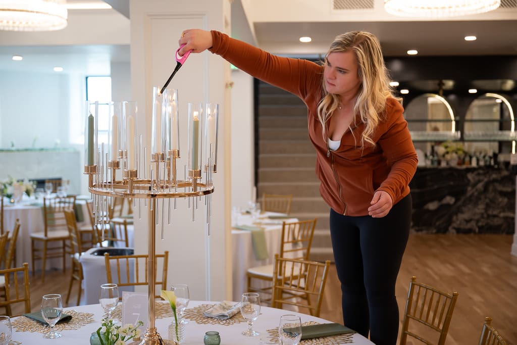 Woman lighting tall candles on a gold candelabra centerpiece before the wedding vendor networking event at Melrose Abbey