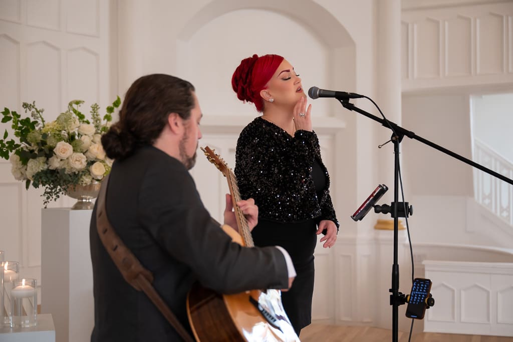 Singer performing at the microphone with a guitarist in the white chapel at Melrose Abbey