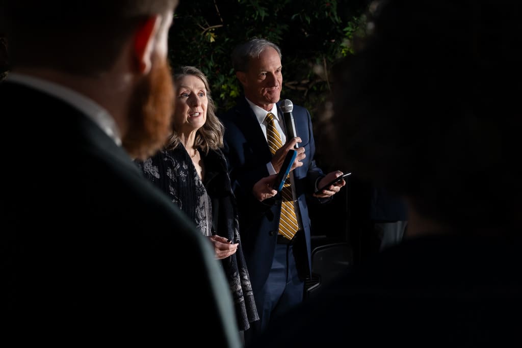 Father of the bride giving a speech as the groom and guests listen in the evening garden
