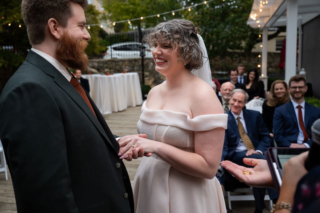 Bride smiling as the groom holds her hands during the ring exchange at an outdoor wedding ceremony at Southmoreland on the Plaza