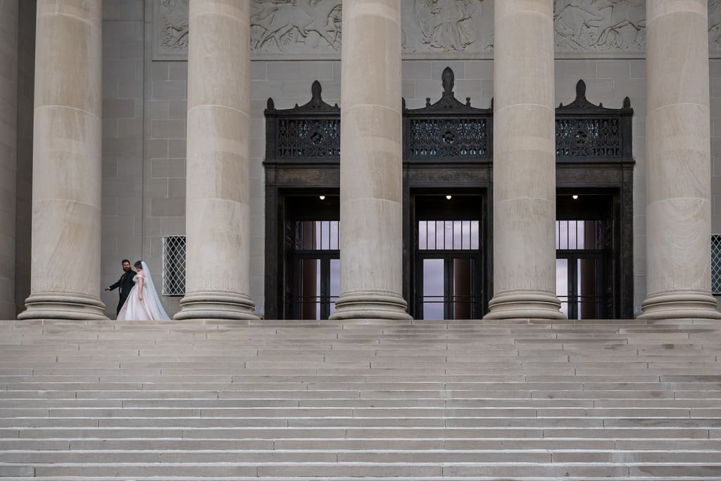 Bride and groom standing small in front of the columns of the Nelson Atkins Museum of Art, Kansas City wedding portrait