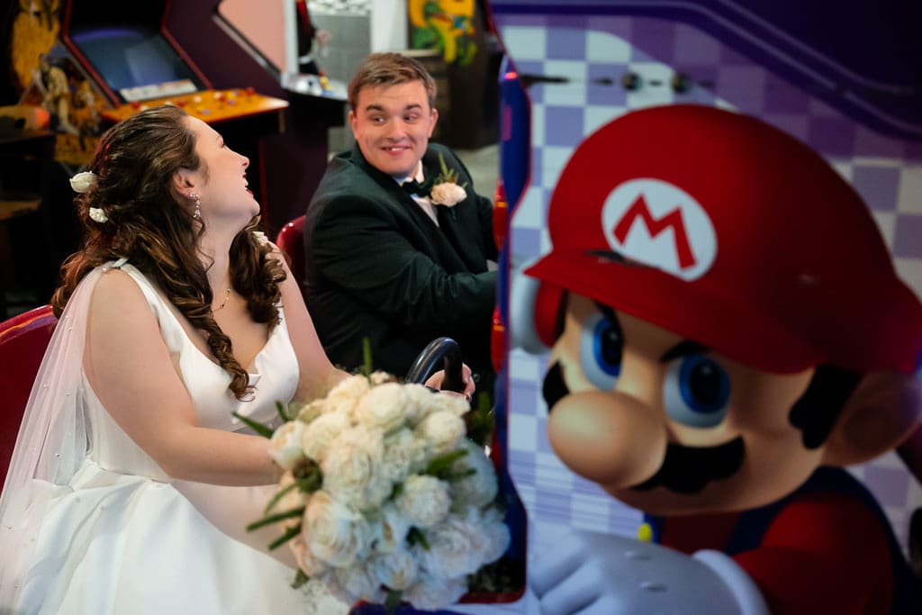Tamieka and Drake play a Mario Kart arcade game at Arcade Alley, her bouquet in her lap