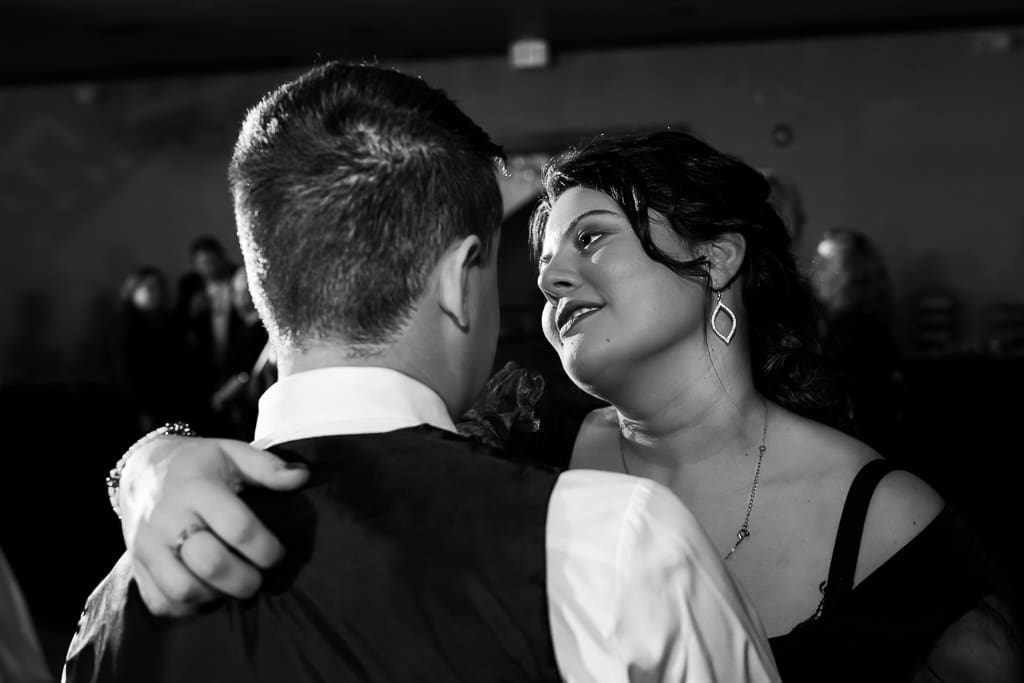 Black and white photo of a couple slow dancing at the reception, she looks up at him smiling