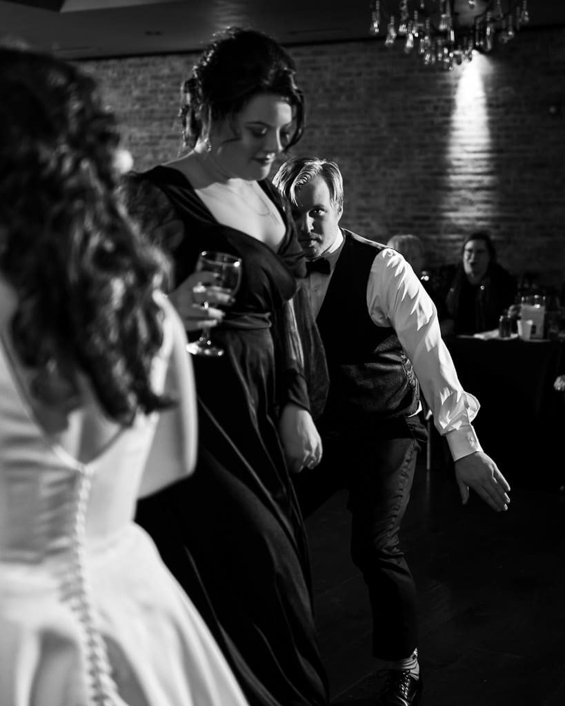 Black and white photo of guests dancing at the reception as Tamieka watches in the foreground