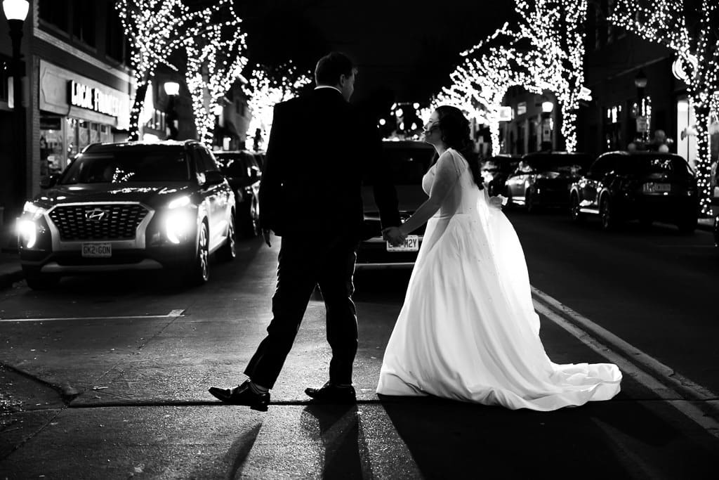 Black and white photo of Drake and Tamieka crossing a street lined with lit trees in downtown Lee's Summit