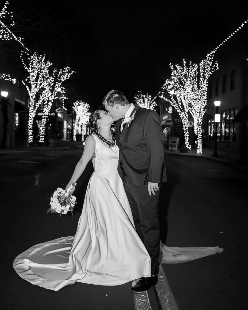 Black and white photo of Drake and Tamieka kissing in the middle of a downtown Lee's Summit street under winter lights